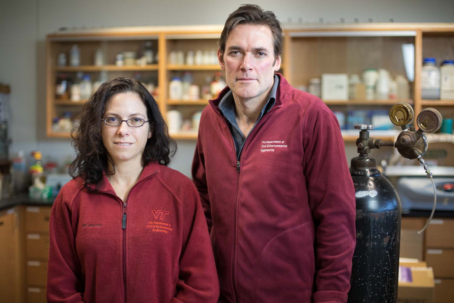 Two faculty stand side by side in a lab setting and smile for a photo.